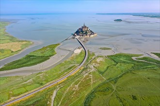 Drone shot of the historic monastery of Le Mont Saint Michel with a view of the salt marshes and the approach dam in the morning light