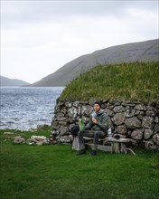 Hiker eating biscuits on a bench in front of a stone hut