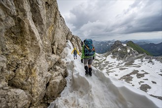 Hiker and hiker on snow remains in rocky terrain