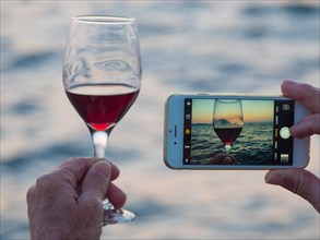 Tourist taking pictures of wine glass and sunset with his smartphone