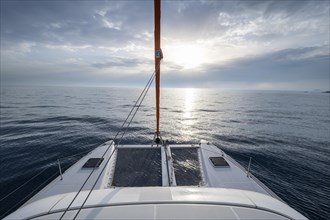Recessed headsail and deck with net of a sailing catamaran in evening light