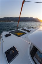 Recessed headsail and deck with net of a sailing catamaran in evening light