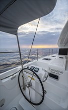 Steering wheel in the cockpit on the deck of a sailing catamaran at sunset