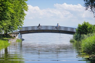 Two cyclists crossing the bridge over the Aach stream at its confluence with Lake Constance