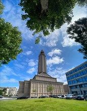 Wide-angle shot of St Joseph's Church with blue sky and framed by trees in Le Havre