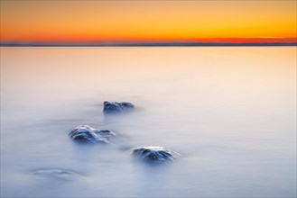 View over Lake Constance at sunrise with stones in the foreground and photographed with slow shutter speed