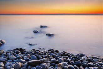 View over Lake Constance at sunrise with stones in the foreground and photographed with slow shutter speed