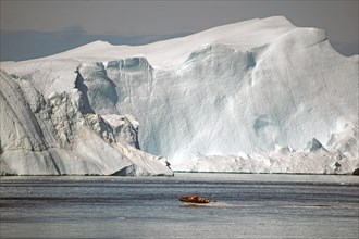 Boat with passengers in front of huge iceberg