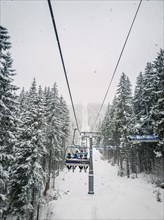 Wonderful winter scene with snow falling while climbing to the top of the mountain on a cable car gondola. Bukovel ski resort in Ukrainian Carpathians. Ski lift passing through the snowy fir forest