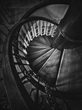 A look down to an old spiral staircase. Wooden circular stairway with ornate metallic railing