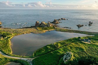 Drone shot from the mainland of the granite coast and the house between the rocks (Le gouffre de Plougrescant) in the morning and the Atlantic Ocean
