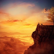 Young man with his faithful dog standing on the peak of a cliff watching the sunset over valley. Recalling childhood memories
