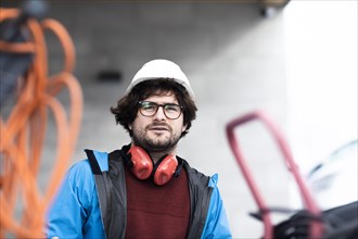 Young engineer with helmet and hearing protection checks outside workplace