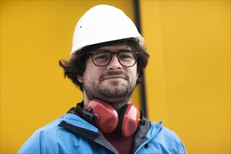 Young engineer with helmet and hearing protection at a work site outside