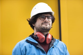 Young engineer with helmet and hearing protection at a work site outside