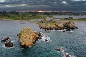 Drone shot from the Atlantic Ocean onto the granite coast of Plougrescant with a view of the house between the rocks (Le gouffre de Plougrescant) at sunset