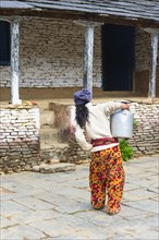 Nepalese woman carrying a metal jug with milk