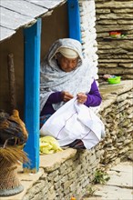 Elderly Nepalese woman sitting in the doorway sewing
