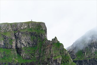 A person stands on a cliff in the distance