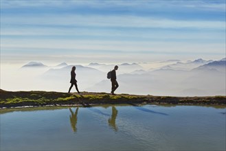 Hikers on a small lake with the peaks of the Lake Garda mountains and Bergamo Alps