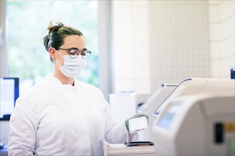 Young lab technician with mouth guard and sample multilayer shell working in a lab with lab equipment