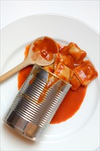 Opened tin can with ravioli and cooking spoon on plate