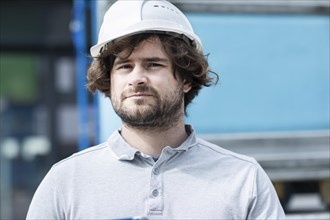 Technician with beard middle aged and wearing polo shirt and helmet outside at work