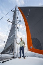 Young man standing between the sails of a sailing catamaran