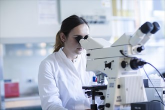 Young laboratory assistant with microscope and sample working in a laboratory with light microscope