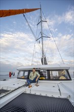 Young man sitting on the deck of a sailing catamaran