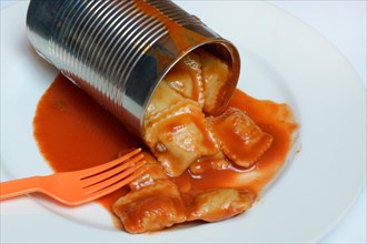 Opened tin can with ravioli and fork on plate