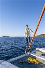 Young man standing by the furled headsail