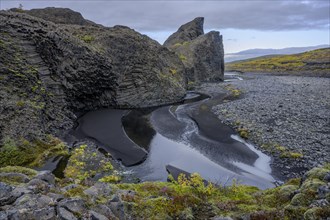 Stream meanders through black lava sand by basalt rocks