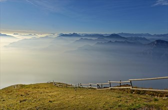 Meadow with fence and Lake Garda in the morning mist with Lake Garda mountains and Bergamo Alps