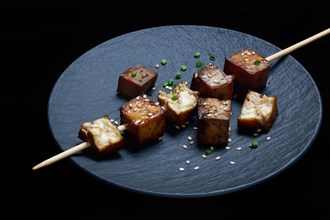 Fried tofu cubes with wooden skewer on plate