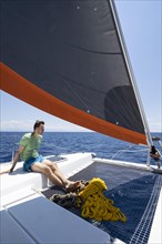 Young man sitting in the net of a sailing catamaran