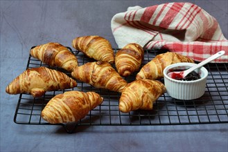 Several croissants on baking rack and bowl with jam