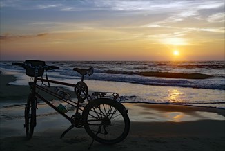 Bicycle on the beach in front of the setting sun