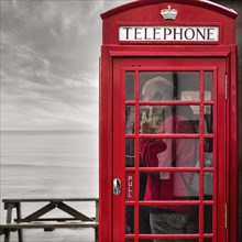 Person talking on phone in red phone box by the sea