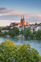 View from the banks of the Rhine along the river promenade to Basel Cathedral and the leafy old town of Basel with the turquoise Rhine River in the foreground