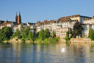 View from the banks of the Rhine along the river promenade to Basel Cathedral and the old town of Basel with the Rhine River in the foreground