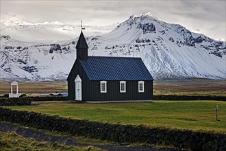 Black wooden church in front of snow-capped mountains