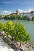 View from the river promenade of Basel Cathedral and the old town of Basel with the turquoise Rhine River and the lively river promenade in the foreground