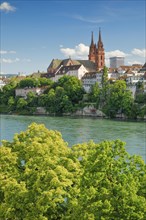 View from the banks of the Rhine along the river promenade to Basel Cathedral and the leafy old town of Basel with the turquoise-coloured Rhine River in the foreground