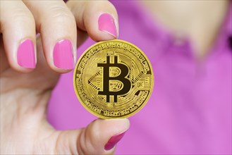 Bitcoin Cryptocurrency coin held between a woman fingers