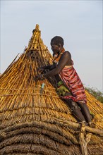 Woman repairing a roof of a traditional build hut of the Toposa tribe