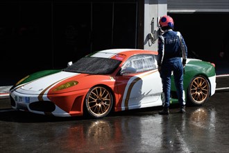 Racing driver looks at Ferrari F430 in design of Italian national flag standing in front of pitbox in pit lane during rain