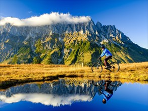 Mountain biker in front of mountain scenery reflected in a mountain lake