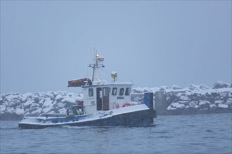 A boat leaves the harbour of Andenes during a snowfall