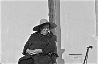 Old woman with folded hands sitting on chair with sun hat